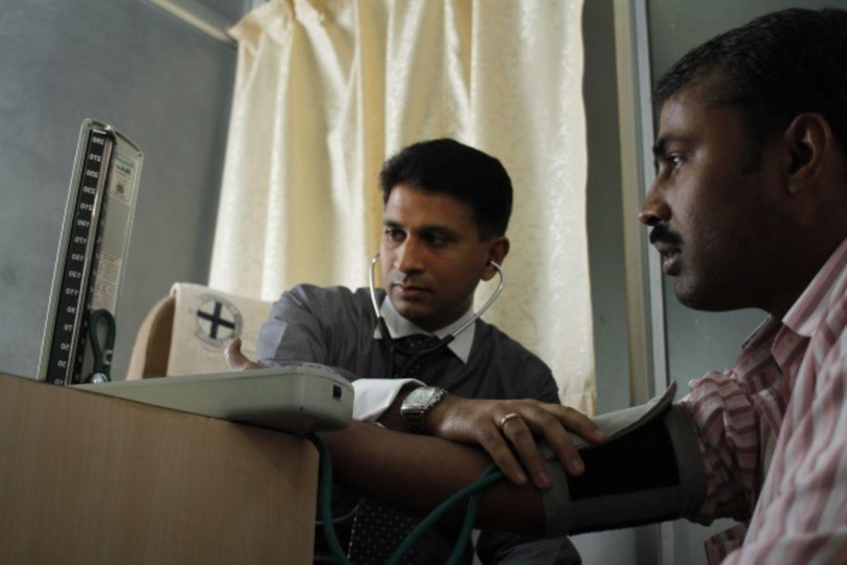 Doctor listening to patient’s pulse with stethoscope as both look at screen.
